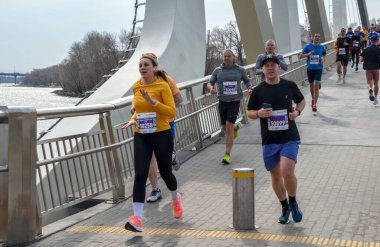 Nehir kenarındaki pitoresk bir köprüde organize bir yarışta aktif olarak koşan çeşitli bireyler.