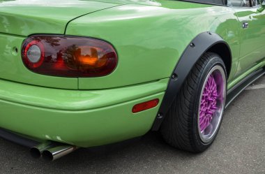 Modifiye edilmiş kireç yeşili Mazda MX-5 Miata 'nın arka görüntüsü geniş siyah çamurluk fişekleri, mor aksanlı bir tekerlek ve çift egzoz boruları sergiliyor.  