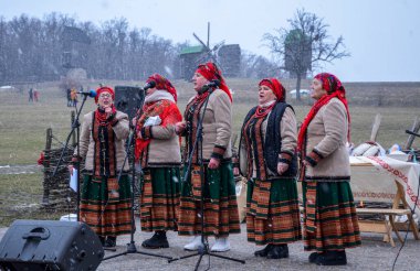 Kültürel giysiler giyen bir grup geleneksel halk şarkıcısı kar yağışı sırasında dışarıda gösteri yapıyor, Shrovetide kutlamaları sırasında kültürel mirası canlandırıyorlar.