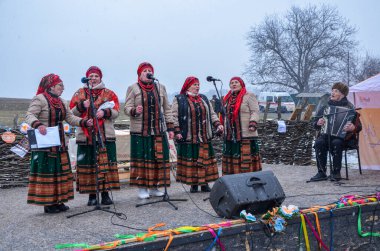 Kültürel giysiler giyen bir grup geleneksel halk şarkıcısı kar yağışı sırasında dışarıda gösteri yapıyor, Shrovetide kutlamaları sırasında kültürel mirası canlandırıyorlar.