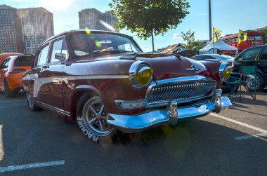 Maroon GAZ-21 Volga, Sovyet döneminin efsanevi otomobili zarif kıvrımlı gövdesi, krom detayları ve geniş dairesel farları ile tanınıyor.