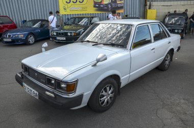 Beyaz Toyota Carina, krom yan aynaları, siyah tamponları ve özgün ön ızgarası ile öne çıkıyor, retro otomotiv estetiğini somutlaştırıyor.