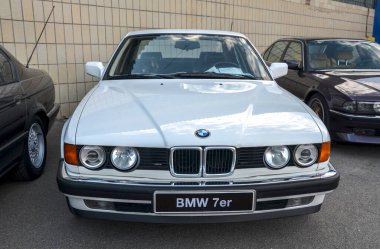 Beyaz BMW 7 Serisi E32, klasik lüks sedan, zamansız tasarımı, gelişmiş teknolojisi ve güçlü motorları var. Alman mühendisliğinin ve idari konforun sembolü