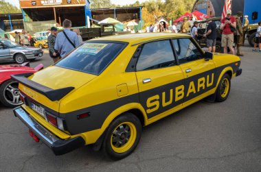 Siyah yarış çizgileri olan sarı Subaru Leone klasik bir kompakt otomotiv kültürü ve Japon işçiliğinin vücut bulmuş halidir.