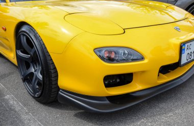 Parlak sarı Mazda RX-7. Simgesel Japon spor arabasının önü odak noktasında, pop-up farları ve parlak tasarımı sergileniyor.