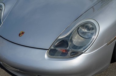 Yakından bakınca gümüş renkli bir Porsche 911 görünüyor. Ana odak noktası ikonik far ve kaputtaki Porsche arması.