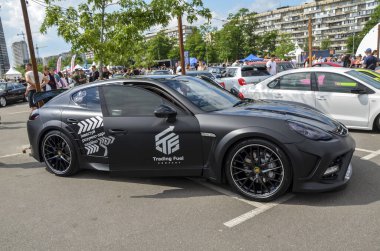 Siyah Porsche Panamera, şık jantları ve renkli camları olan, bir araba etkinliğinde sergilenen. Lüks bir spor sedan. Performans, zarafet ve kişiselleştirme çekiciliği harmanlıyor.