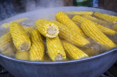 Sıcak altın mısır koçanları buharda pişiriliyor, taze ve sağlıklı atıştırmalıklar sergileniyor. Gelenek ve tat karışımı bu lezzetli görüntüde sergileniyor, mutfak malzemeleri için mükemmel.