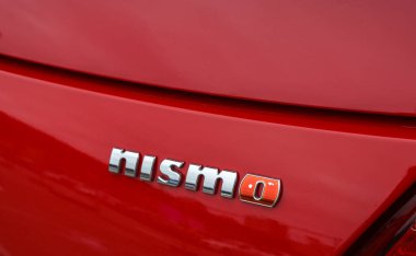 Kırmızı bir Nissan arabanın arkasında gümüş renkli bir Nismo rozet sergileniyor. Otomotiv detay çekimi