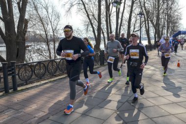 Katılımcılar, berrak bir gökyüzünün altında nehir kenarındaki bir patika boyunca yarışarak enerji ve başarı atmosferi yaratıyorlar.
