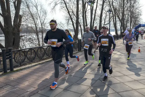Katılımcılar, berrak bir gökyüzünün altında nehir kenarındaki bir patika boyunca yarışarak enerji ve başarı atmosferi yaratıyorlar.