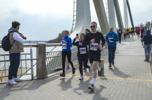 Nehir kenarındaki köprüde birlikte maraton koşan atletik bireyler, şehir ortamında spor ve takım çalışması sergiliyorlar.