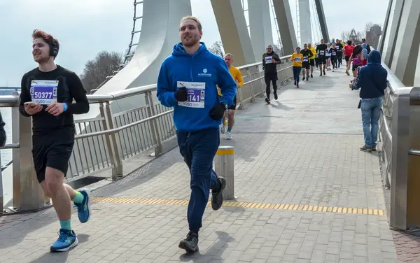 Nehir kenarındaki köprüde birlikte maraton koşan atletik bireyler, şehir ortamında spor ve takım çalışması sergiliyorlar.