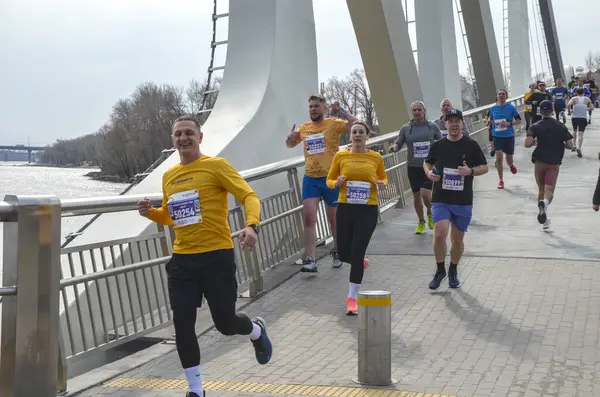 Nehir kenarındaki köprüde birlikte maraton koşan atletik bireyler, şehir ortamında spor ve takım çalışması sergiliyorlar.