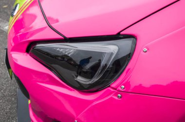 Yakın plan, parlak pembe modifiye Subaru BRZ arabasında parlak siyah far ve perçinli geniş çamurluk fişekleri gösteriyor.