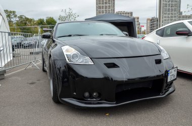 Parlak siyah Nissan 350Z, özel tampon ve sis lambalı. Düşük duruş, pazardan sonraki tekerlekler ve agresif stil otomotiv meraklıları için dikkat çekiyor.