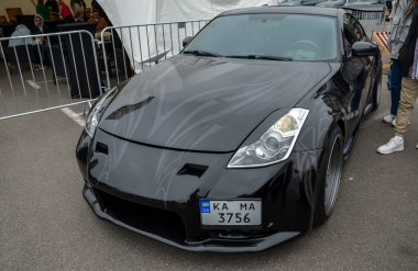 Parlak siyah Nissan 350Z, özel tampon ve sis lambalı. Düşük duruş, pazardan sonraki tekerlekler ve agresif stil otomotiv meraklıları için dikkat çekiyor.