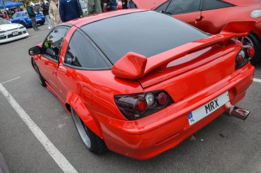 Çarpıcı kırmızı Mitsubishi Eclipse, ön tamponu geliştirilmiş ve ön tamponu cesur ve sportif bir görünüme göre modifiye edilmiş, bir araba sergisinde sergileniyor.