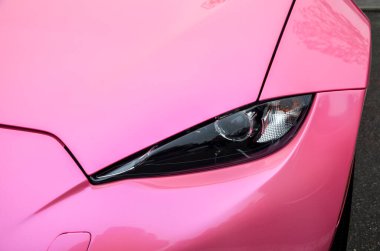 Parlak pembe Mazda MX-5 'in ön köşesinin yakın görüntüsü, far ve kaputun düz kıvrımları ve çamurluğun keskin tasarımını vurguluyor. 
