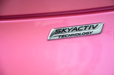Arabanın parlak pembe kaportasında Skyactiv Teknoloji rozetinin yakın plan görüntüsü. Gümüş amblem parlak boyaya karşı duruyor.