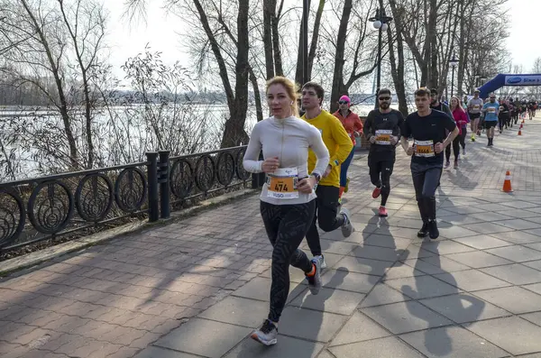 Koşucular canlı bir açık hava yarışına aktif olarak katılıyorlar. Nehir manzaralı ve ağaçlarla çevrili. 