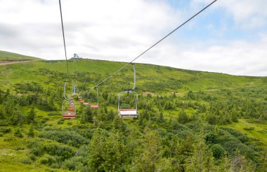 Bereketli yeşil bir manzaranın üzerinde, canlı tepeler, canlı bitki örtüsü ve sakin bir çevreye sahip, açık hava keşiflerini, doğayı ve rahatlamayı sembolize ediyor.