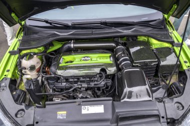 Canlı yeşil ve siyah özelleştirilmiş Volkswagen otomobil motor bölmesi, karbon fiber elementler ve belirgin bir VW logosu ile gösteriliyor