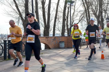 Bir grup atletizm sporcusu nehir kenarındaki patika boyunca maratona katılıyor. Koşucular, barışçıl bir günde açık hava fitness etkinliği sırasında kendilerini adamış ve enerjik görünüyorlar.