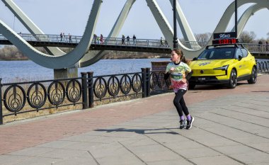 Kentsel bir çevrede düzenlenen bir spor etkinliği sırasında nehir kenarında koşan genç bir sporcu kız.