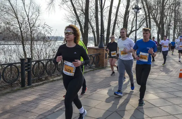 Bir grup atletizm sporcusu nehir kenarındaki patika boyunca maratona katılıyor. Koşucular, barışçıl bir günde açık hava fitness etkinliği sırasında kendilerini adamış ve enerjik görünüyorlar.