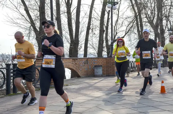 Bir grup atletizm sporcusu nehir kenarındaki patika boyunca maratona katılıyor. Koşucular, barışçıl bir günde açık hava fitness etkinliği sırasında kendilerini adamış ve enerjik görünüyorlar.