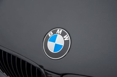 Koyu renkli bir arabanın BMW ambleminin yakın çekimi, ikonik mavi ve beyaz yuvarlak