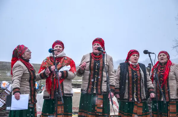 Renkli giysiler içinde bir grup geleneksel folk şarkıcısı dışarıda karlı zemine karşı gösteri yapıyor. Kültürel birlik, kutlama ve ahenk duyguları uyandırıyor.