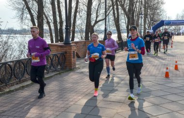 Bir grup koşucu, doğa tarafından çevrelenmiş nehir kenarındaki yürüyüş yolu boyunca düzenlenmiş bir açık hava etkinliğine katılıyor.