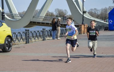 Bir grup sporcu, gündüz düzenlenen bir maraton sırasında nehir kenarında manzaralı bir patika boyunca koşuyor.