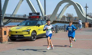 Bir grup sporcu, gündüz düzenlenen bir maraton sırasında nehir kenarında manzaralı bir patika boyunca koşuyor.