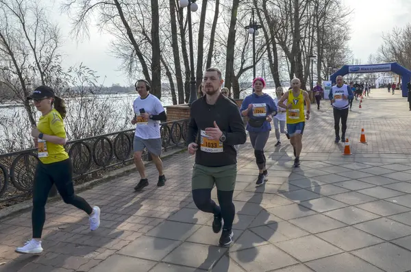Bir grup koşucu, doğa tarafından çevrelenmiş nehir kenarındaki yürüyüş yolu boyunca düzenlenmiş bir açık hava etkinliğine katılıyor.