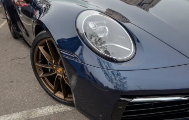Koyu mavi Porsche 911 'in ön çeyreğine yakın plan, ikonik yuvarlak farını gösteriyor ve bronz renkli çok dilli tekerleği vuruyor.
