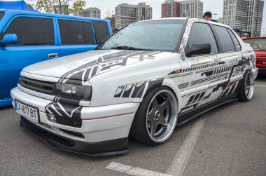 Beyaz Volkswagen Vento (Golf Mk3) sedan çarpıcı siyah, altın ve beyaz grafik çıkartmalı, özel tekerli ve düşük süspansiyonlu, açık hava araba etkinliğinde park edilmiş