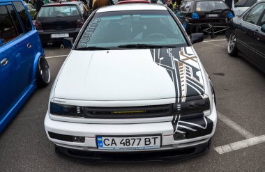 Beyaz Volkswagen Vento (Golf Mk3) sedan çarpıcı siyah, altın ve beyaz grafik çıkartmalı, özel tekerli ve düşük süspansiyonlu, açık hava araba etkinliğinde park edilmiş