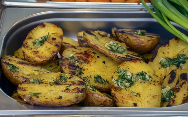 Lezzetli ızgara patatesler taze bitkisel tereyağıyla süslenmiş, paslanmaz çelik servis tepsisinde sunuluyor. Mutfak sunumları, yemek içeriği ya da sağlıklı yemekler için ideal.