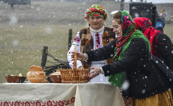 Renkli geleneksel giysiler giymiş kadınlar kar yağarken, kültürel gelenekleri sergilerken ve topluluk masanın etrafında toplanırken açık havada kutlama yapıyorlar. 