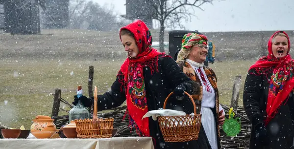 Renkli geleneksel giysiler giymiş kadınlar kar yağarken, kültürel gelenekleri sergilerken ve topluluk masanın etrafında toplanırken açık havada kutlama yapıyorlar. 