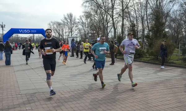 Maraton katılımcıları bir park yolu boyunca koşuyor, atletik dayanıklılık, kararlılık ve açık hava aktivitesi sergiliyorlar.
