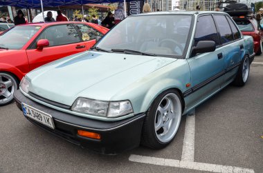 Açık yeşil özel yapım Honda Civic (dördüncü nesil EF sedan), düşük süspansiyonlu ve market sonrası tekerlekleriyle bir açık hava otomobil fuarına park edilmiştir. Klasik JDM Biçimi