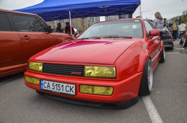 Canlı kırmızı Volkswagen Corrado 1990, sarı farlar ve düşük süspansiyonlu açık hava otomobil etkinliğinde gösteriliyor.