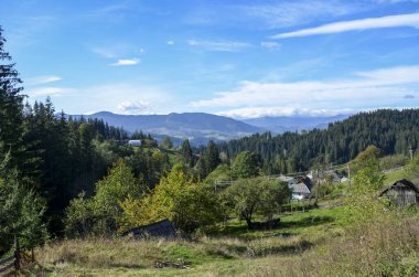 Dağ köyünün sakin kırsal manzarası. Parlak mavi gökyüzünün altındaki yemyeşil alanlar ve ormanlarla çevrili. Doğal ve barışçıl ortamda kırsal yaşamın güzelliğini gözler önüne seriyor. Karpatlar, Ukrayna
