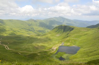 Huzurlu dağ vadisinde canlı yeşil çayırlar, dolambaçlı yollar ve bulutlu bir gökyüzünün altında sakin bir Dogyaska gölü bulunur. Svydovets, Karpatlar, Ukrayna