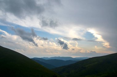 Yumuşak tepe yamaçlarının, sık ormanların, gün ışığının ve bulutlu gökyüzünün olduğu sakin bir manzara. Karpat Dağları, Ukrayna 