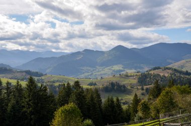 Bereketli yeşil yamaçlar, uzak tepeler ve parçalı bulutlu gökyüzünün altındaki uçsuz bucaksız yeşil ormanların yer aldığı dağ vadisinin nefes kesici manzarası. Karpat Dağları, Ukrayna  